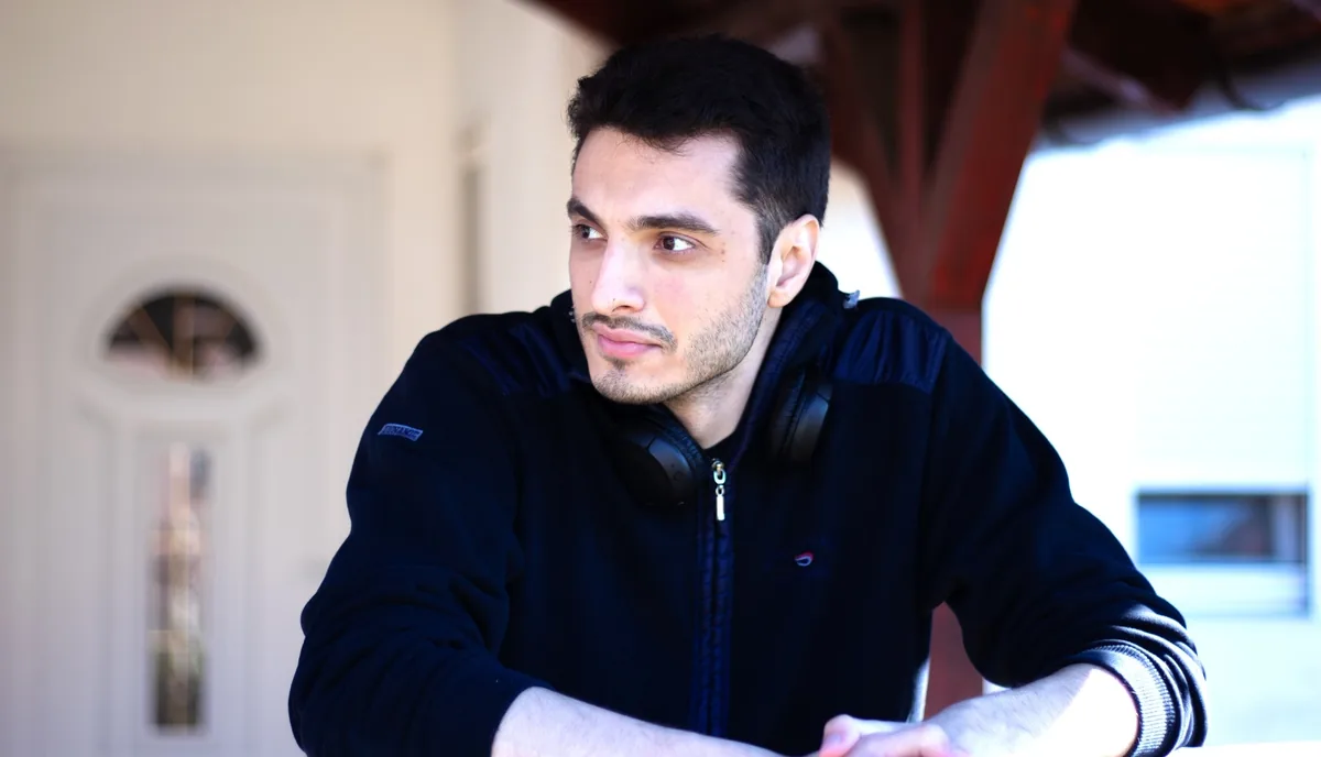 Milos Brakus in a dark jacket with headphones around his neck, looking off-camera in warm natural light.